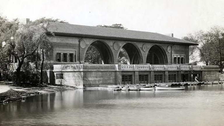 Historic photograph of a boathouse with arched openings on the water with rowboats docked.