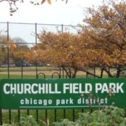Churchill Field Park sign in Chicago, with a field, chain link fence, and fall trees in the background.