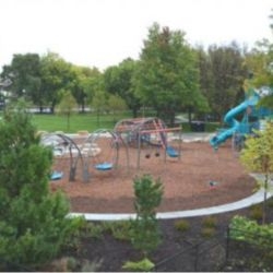 Playground with swings and slides surrounded by trees and shrubs.