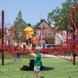 Children play on a red climbing net at a park.