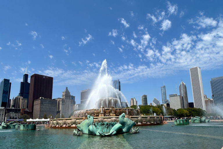 Buckingham Fountain spraying water with the Chicago skyline in the background on a partly cloudy day.