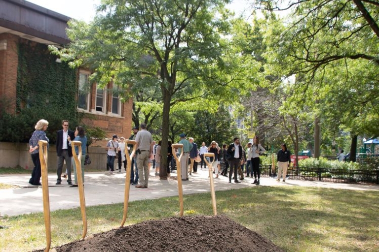 Group gathers for groundbreaking ceremony near building and park.