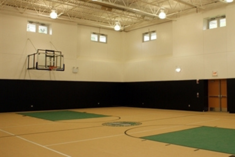 Empty indoor basketball court with tan floor and dark lower walls.
