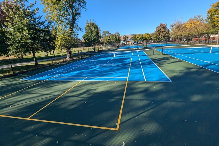 Empty blue and green tennis and pickleball courts on a sunny autumn day.