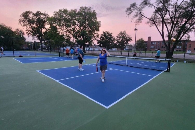 People playing pickleball on blue and green courts at sunset.