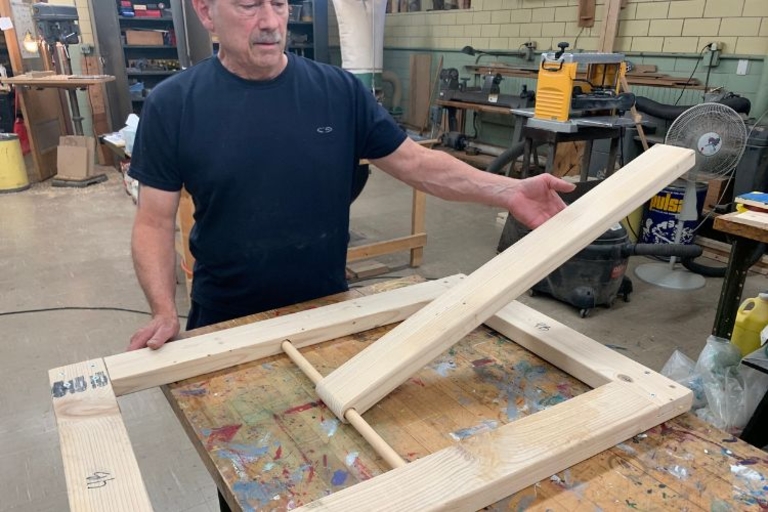 Man demonstrates the movement of a wooden lever attached to a larger wooden frame.