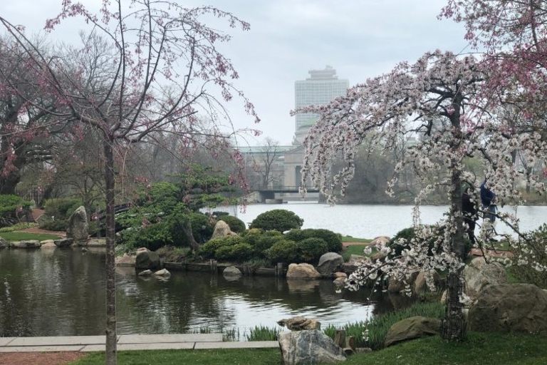 Japanese garden with blossoming trees, pond, bridge, and building in the background.