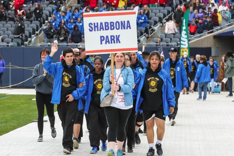 Group walks on stadium track carrying "Shabbona Park" sign.
