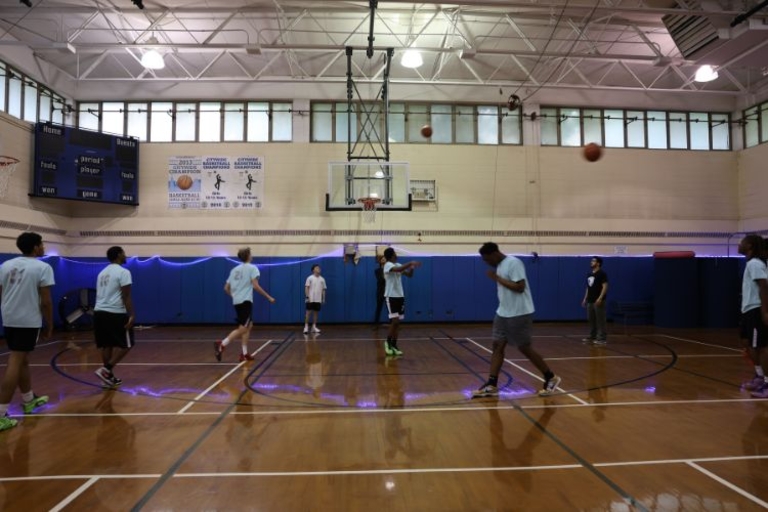 Basketball players scrimmage on a shiny wooden court in a gym.