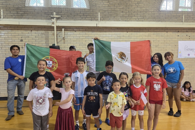 Children and adults hold flags from different countries in a gymnasium.