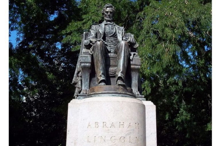 Bronze statue of Abraham Lincoln seated in a large chair, on a pedestal, with trees behind.
