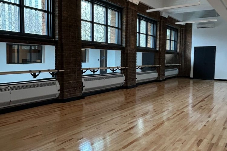 Empty dance studio with barres, wood floor, and large windows.