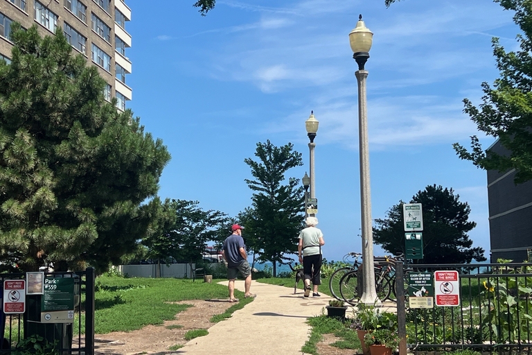 Two people walk on a paved path in a small park near a tall building and Lake Michigan.