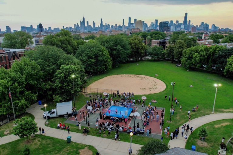 Outdoor boxing match in a city park, Chicago skyline in the background.