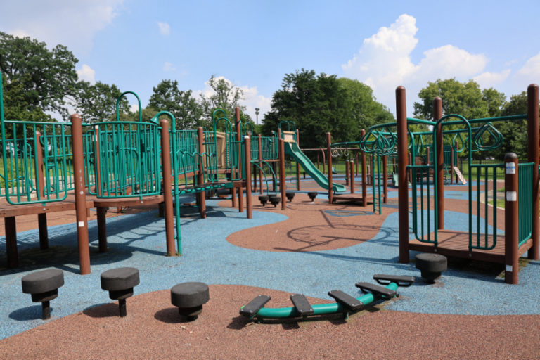 A playground with green and brown structures on a colorful, poured-in-place safety surface.