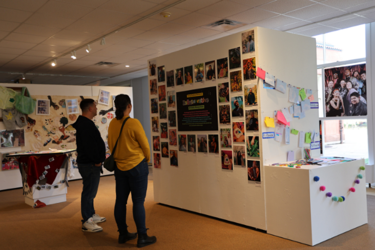 People viewing a gallery wall of photographs and colorful sticky notes.