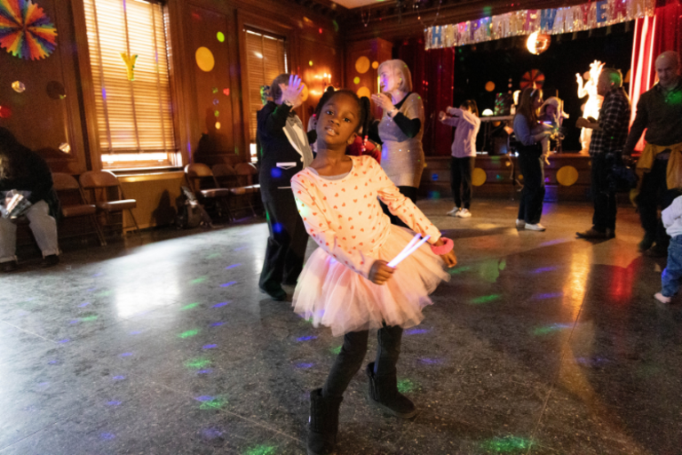 Photograph of a child in a tutu dancing at a party.