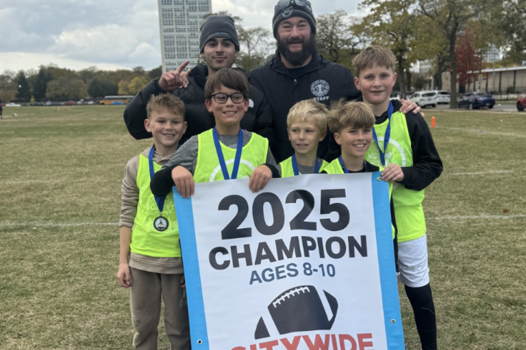 Champions smiling with 2025 champion banner, outdoors.
