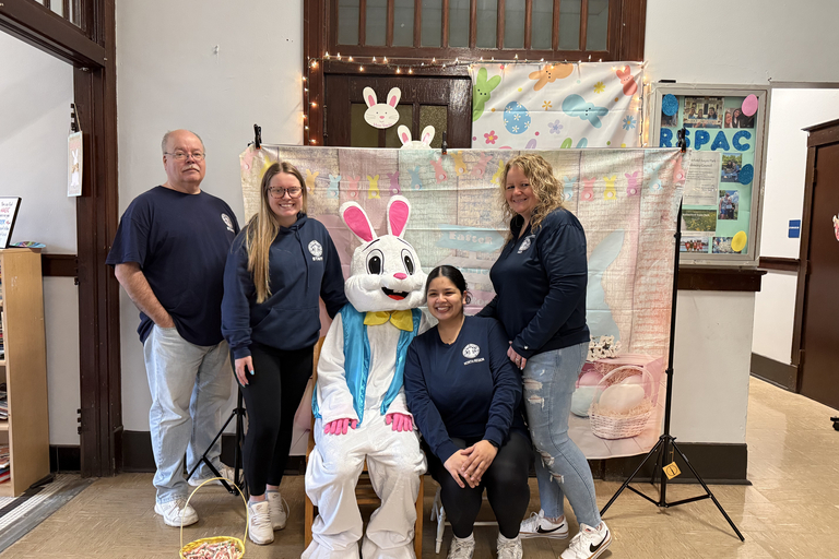 Four staff members pose with an Easter Bunny mascot in front of a decorative holiday backdrop.
