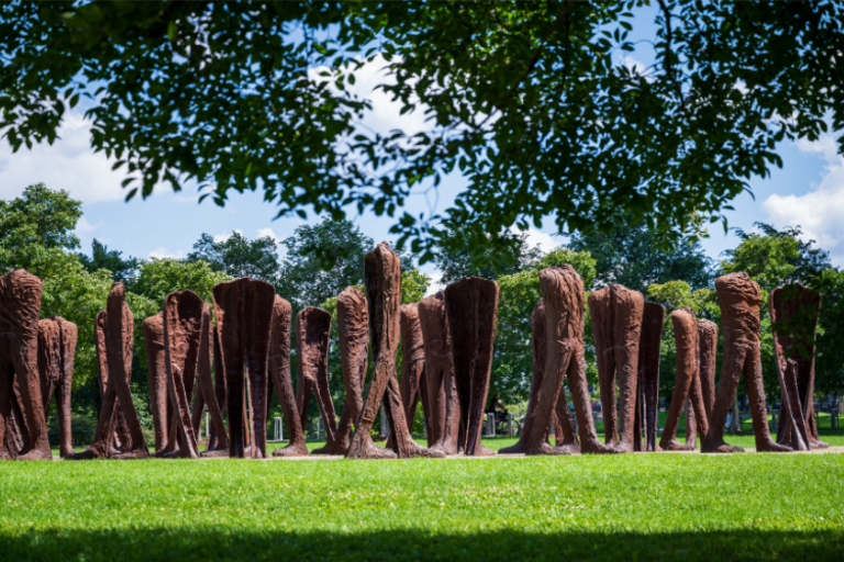 Photograph of a sculpture installation of multiple abstract metal legs standing on green grass.