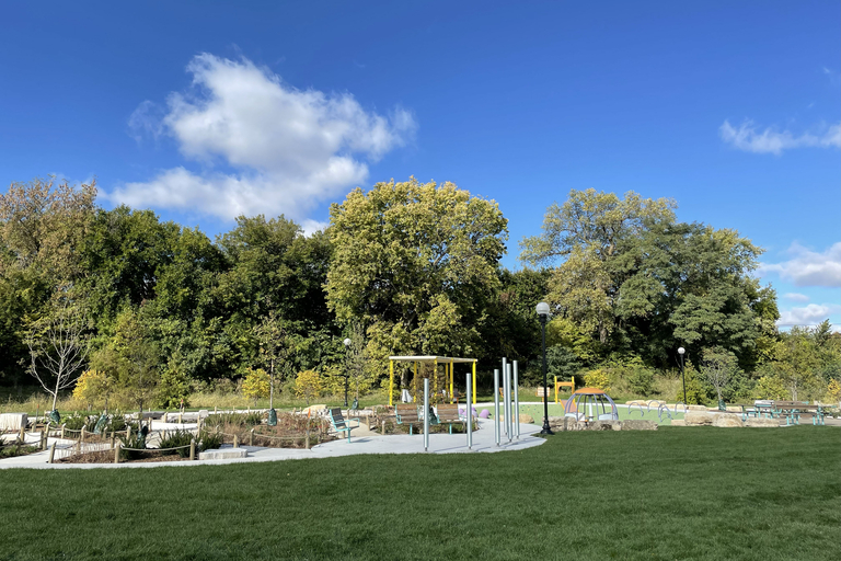 A sunny park features a grassy lawn, musical instruments, benches, and trees under a blue sky.