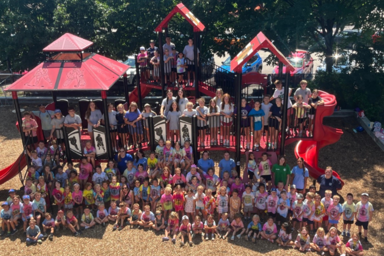 A large group of children and camp counselors posing together on a red playground structure.