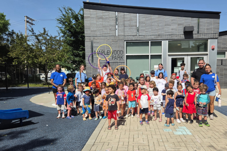 Group of children and adults posing for a photo in front of the Maplewood Park community building.