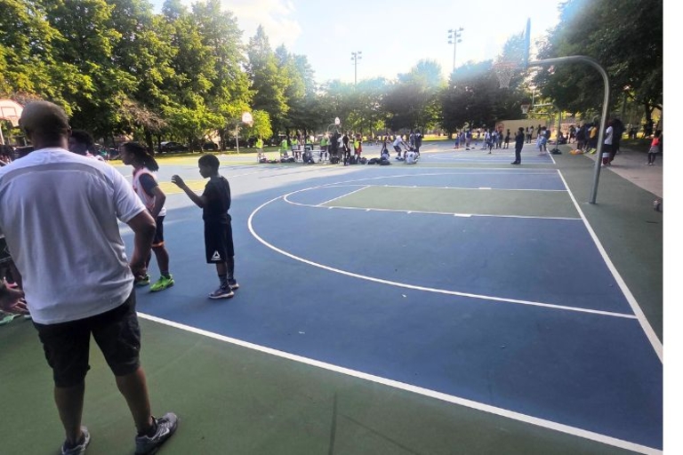 Photograph of people playing basketball on an outdoor court at a park.