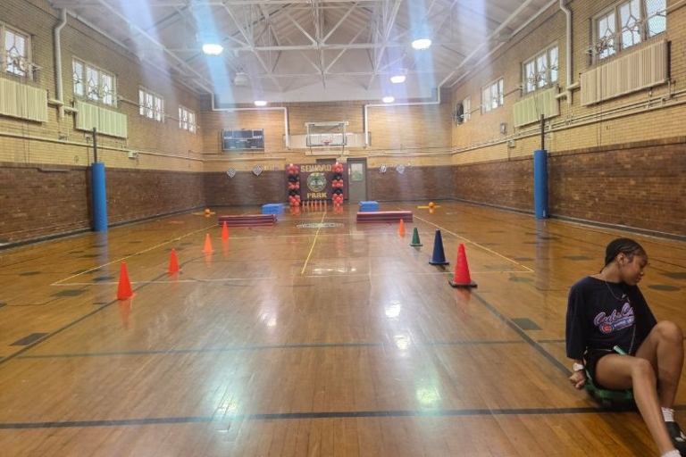 Photograph of a school gym with floor cones and a seated student.