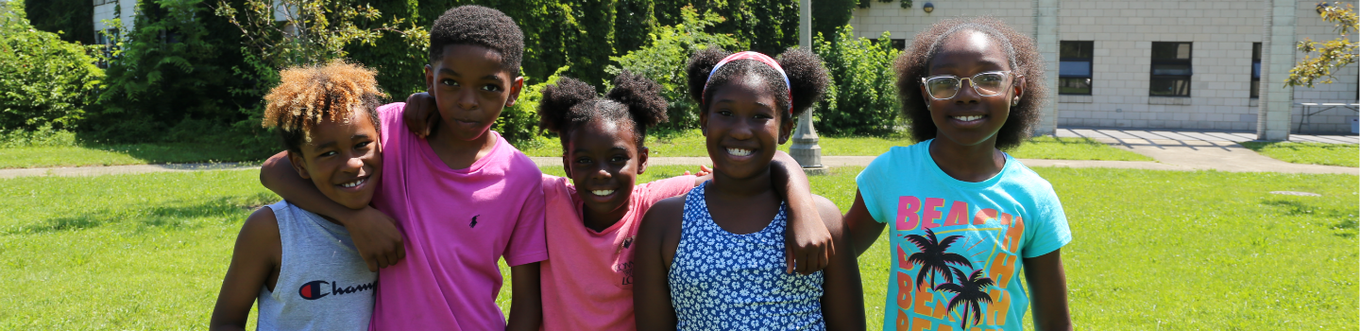 Five children with arms around each other smile at the camera in a park.