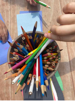 A hand picks a colored pencil from a container of various colored pencils.