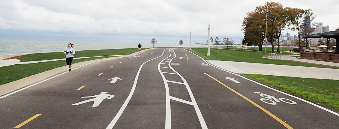 Paved path along lakefront with pedestrian and bike lanes. People jogging.