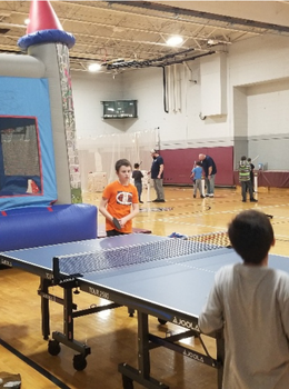 Two boys playing ping pong in a gym.