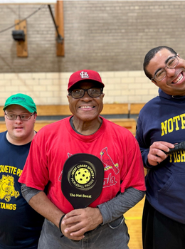 Three smiling pickleball players in a gym.