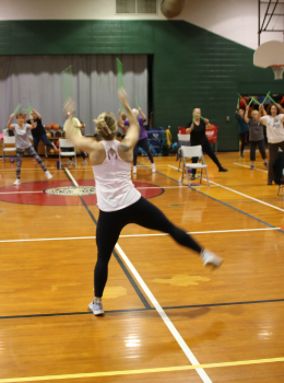 Instructor leads a choreographed exercise class using green foam swords.