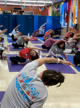 Children and an instructor practice a seated spinal twist yoga pose.