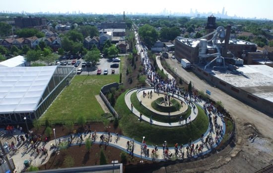 Aerial view of cyclists on a winding path around a spiral hill in an urban park.