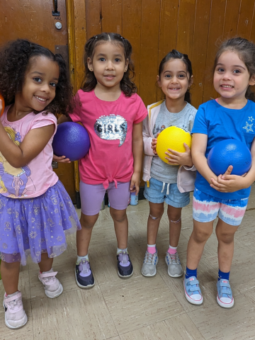 Four young girls holding playground balls, smiling for the camera.
