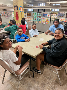 Kids and adults crafting at a table, smiling at the camera.