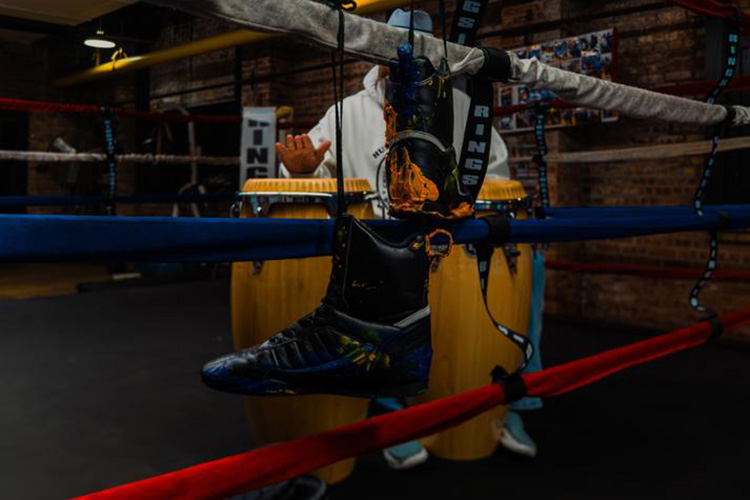 Pair of custom boxing shoes hang on boxing ring ropes.