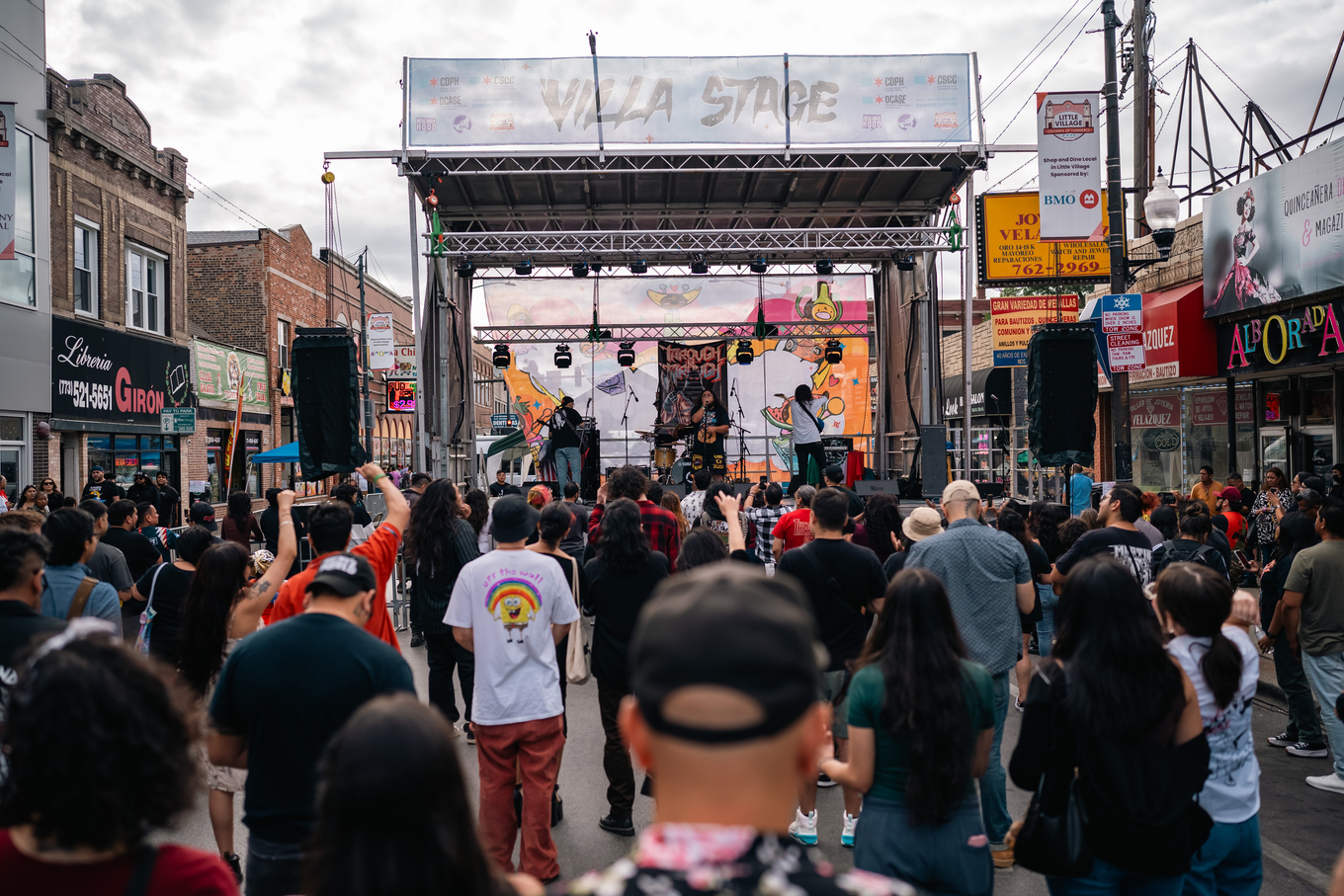 Crowd watches band perform on outdoor stage at street festival.