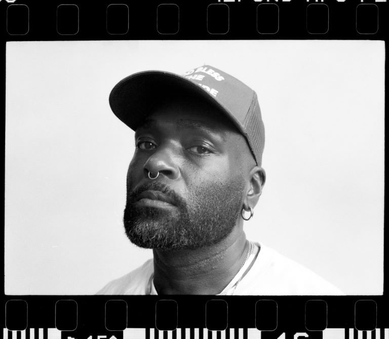 Black and white photo of a person wearing a baseball cap and a septum piercing.