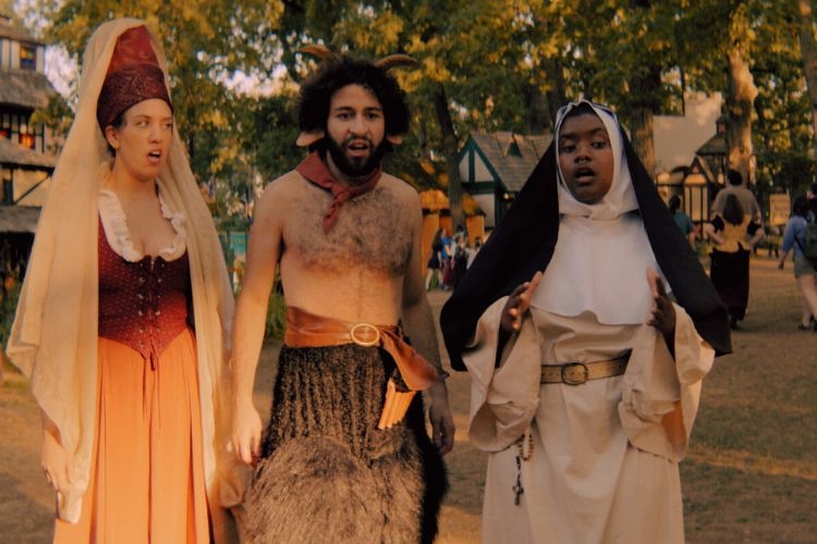 Three people in Renaissance costumes: a woman, a satyr, and a nun, appear surprised.