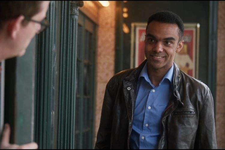 Man in leather jacket smiles at another man.