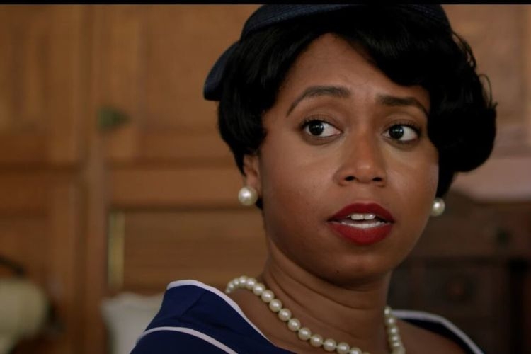 Woman wearing a hat, pearl earrings and necklace looks off to the side.