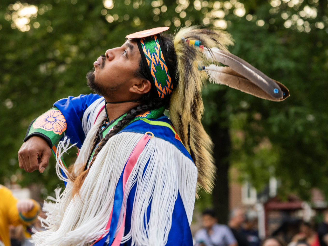 Indigenous dancer wearing colorful regalia looks upward.