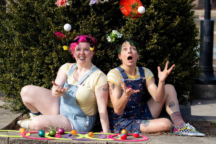 Two clowns juggling various objects with surprised expressions.