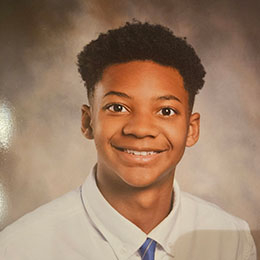 Smiling young Black man in school photo wearing white shirt and tie.