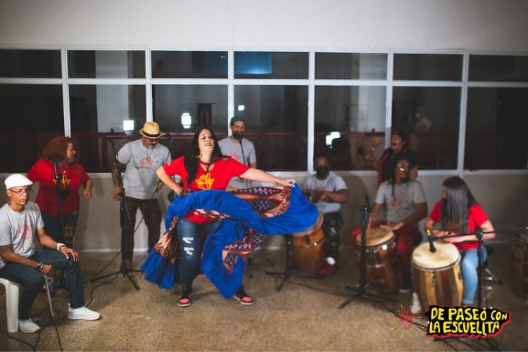 Musicians play drums as woman dances in flowing blue skirt.