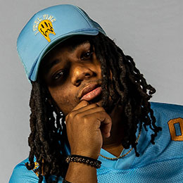 Young man wearing a light blue baseball cap and matching football jersey, hand on chin.